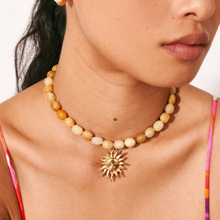 Close-up of a collarbone wearing a honey-toned bead choker with a gold sun pendant – bestsellers by Love Letter