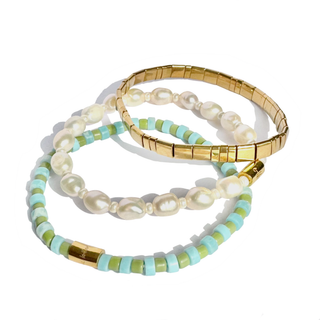 Three beaded bracelets arranged on a white background: one gold-toned bangle, one strand of white baroque pearls with light blue beads, and one strand of light green and light blue beads with gold-toned spacer accents.