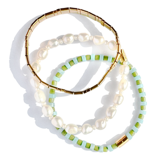 Three beaded bracelets arranged in a circle on a white background. One bracelet is gold with white baroque pearls, one is white with white pearls, and one is light blue and green with gold accents.