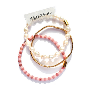 Three beaded stretch bracelets arranged in a stack on a white background. The top bracelet features irregular white pearls, the middle bracelet has gold-toned metal bands with small pink beads, and the bottom bracelet is made of pink faceted beads.