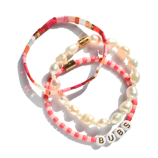 Three beaded stretch bracelets stacked together on a white background. The bracelets feature pink, coral, and orange beads, white pearl-like beads, and one bracelet has white letter beads spelling 'BUBS'.