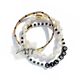 Three stacked beaded bracelets on a white background. One bracelet features irregular white baroque pearls with black and gold spacer beads.
