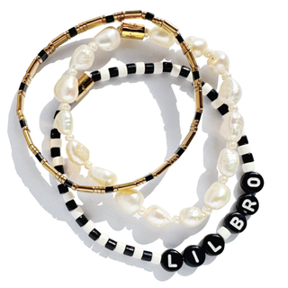 Three beaded bracelets stacked together on a white background. One bracelet features irregular white baroque pearls, another has black and white beads, and the third is gold with black beads spelling 'LIL BRO'.