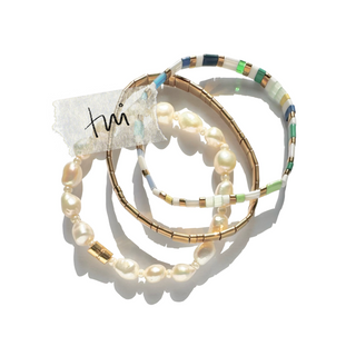 Three stacked beaded and pearl bracelets on a white background, featuring gold-toned metal, cream pearls, and colorful beads in green, blue, white, and gold.